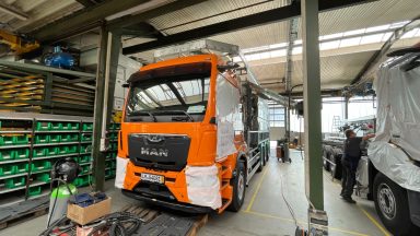 Orange Lkw in einer Werkstatt mit Werkzeug und Arbeitsbereichen im Hintergrund.